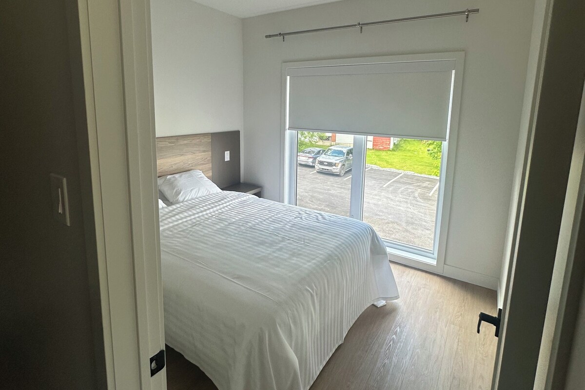 A bedroom with a bed, a window with a view of the outside, and a ceiling light.