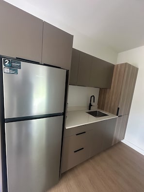 A compact kitchen with a stainless steel refrigerator, a sink, and wooden cabinets. - Hotel W Des Cantons (Weedon)