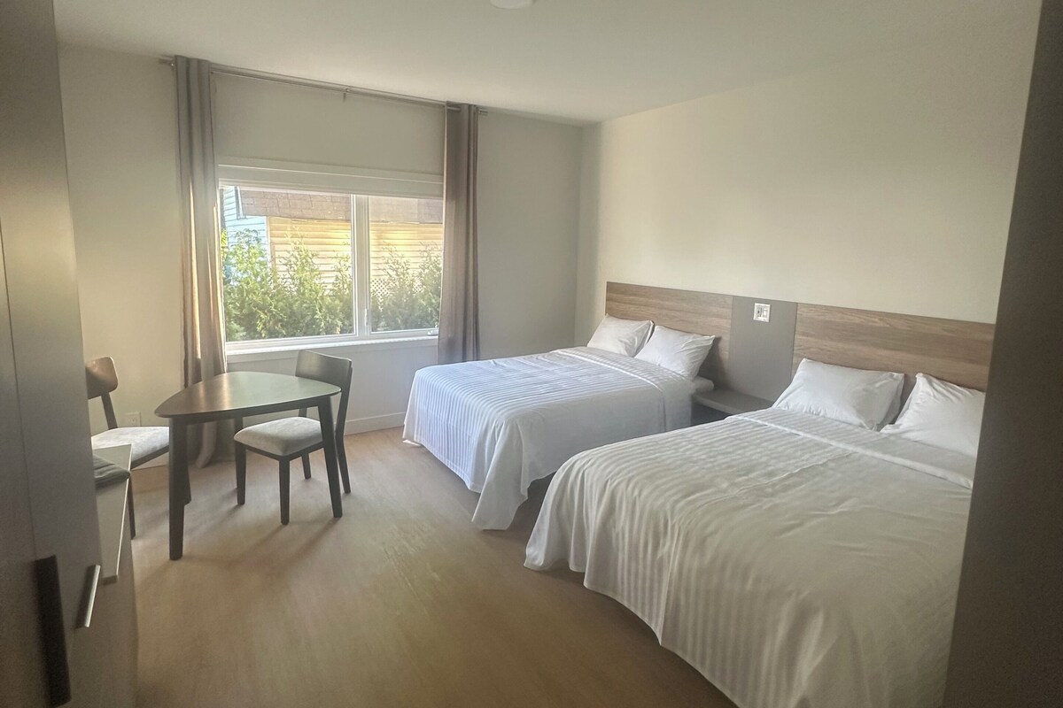 A hotel room with two beds, a dining table, and a window with curtains.