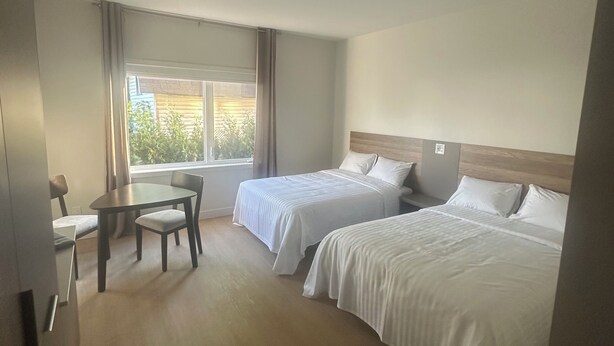 Una habitación de hotel con dos camas, una mesa de comedor y un ventanal con cortinas.