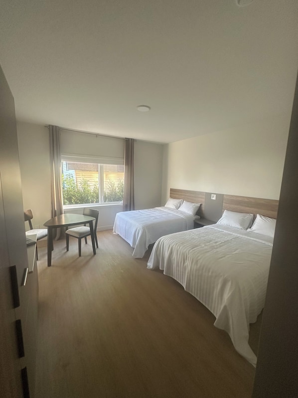 A hotel room with two beds, a dining table, and a window with curtains. - Hotel W Des Cantons (Weedon)
