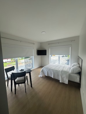 A bedroom with a bed, a TV, a table, and chairs. - Hotel W Des Cantons (Weedon)