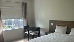 Una habitación de hotel con cama, escritorio, silla y ventana con cortinas.