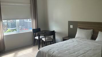 Una habitación de hotel con cama, escritorio, silla y ventana con cortinas.
