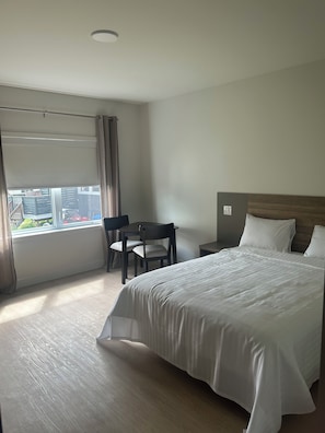 A hotel room with a bed, a desk, a chair, and a window with curtains. - Hotel W Des Cantons (Weedon)