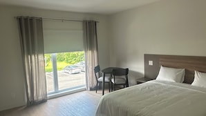 Habitación de hotel con una cama grande, un escritorio con dos sillas, vista a través de un ventanal y piso de madera.