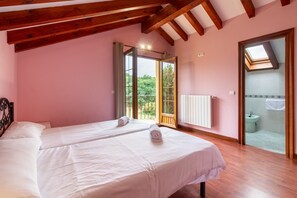 Une chambre avec deux lits, des poutres en bois, des murs roses, une lucarne et une salle de bain visible à travers une porte ouverte.