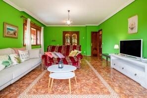 Ein Wohnzimmer mit einer Couch, einem roten, gemusterten Sofa, einem Fernseher und einer Kandelaber.