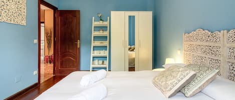 A bedroom with a bed, a wardrobe, a shelf with decorative items, and a door leading to another room.