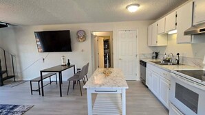 Una cocina moderna con armarios blancos, encimera de mármol y un comedor con mesa y sillas.