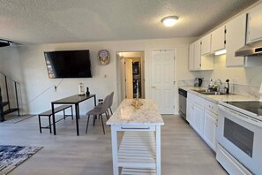 A modern kitchen with white cabinets, a marble countertop, and a dining area with a table and chairs. - Cozy 2BR Retreat | King Bed | Private Deck | AC (Auburn)