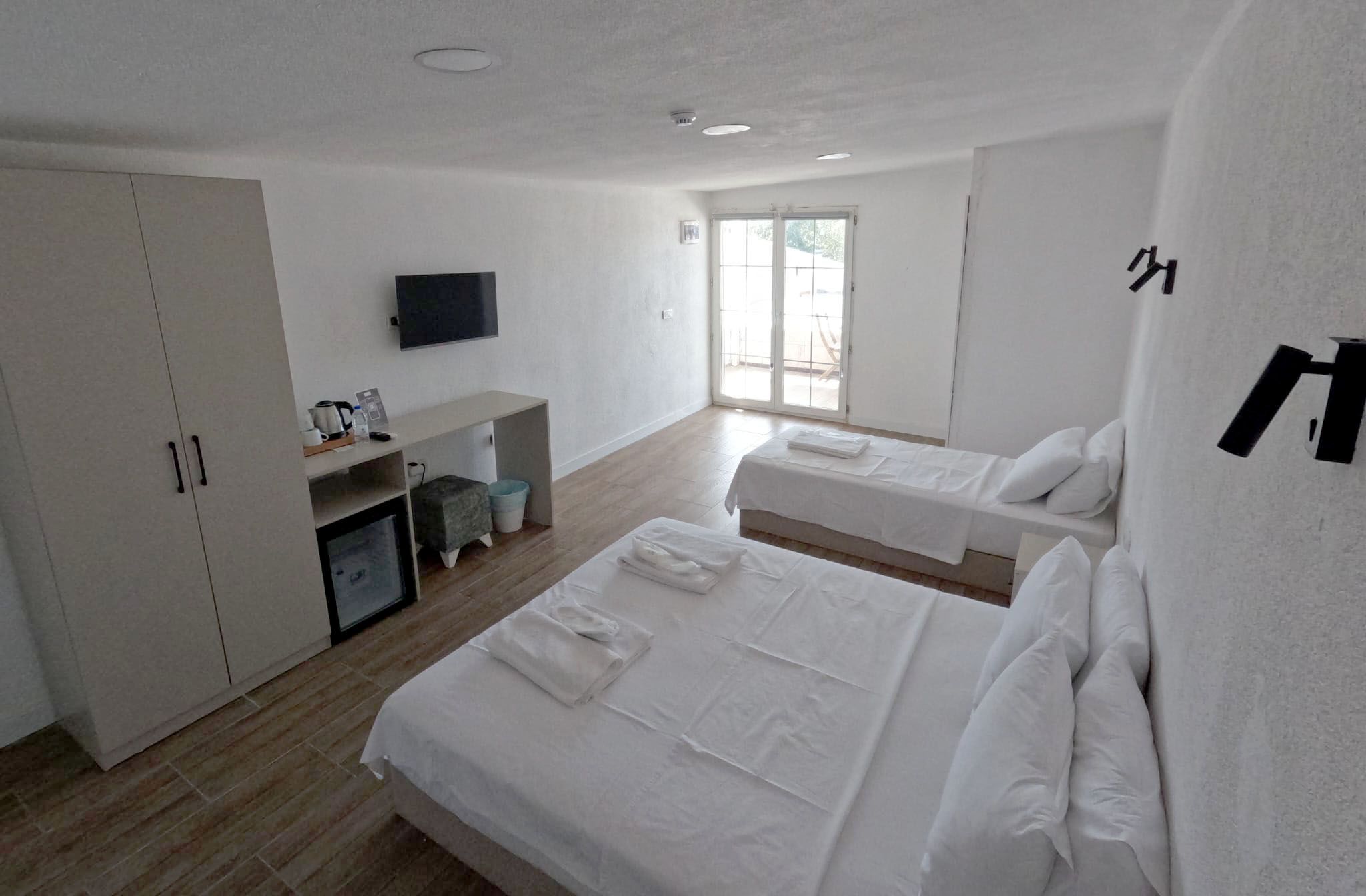 Ein modernes Schlafzimmer mit zwei Betten, einem Fernseher und einer Schiebetür zum Balkon.