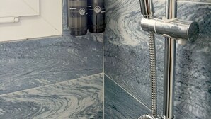 A modern bathroom with a shower, marble tiles, and two shampoo bottles. - Suda Pansiyon (Bodrum)