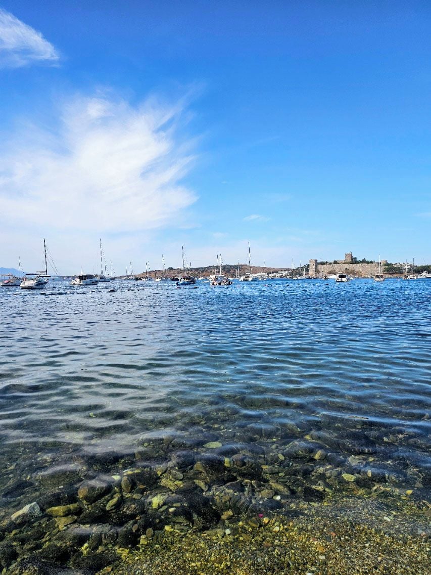 Eine Küstenlandschaft mit klarem Wasser, Booten und einer im Hintergrund liegenden, festungsähnlichen Struktur.