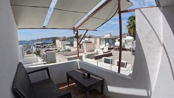 Un balcón con mesa y sillas, con vista a una zona costera con edificios y barcos.