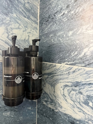 Two black bottles with pump dispensers, labeled 'Sampuan,' against a marble wall.