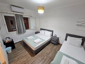 A bedroom with a bed, bedside tables, a nightstand, a window with curtains, and a wall-mounted air conditioner.