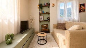 Un salon avec un canapé, un téléviseur posé sur un meuble, une petite table et une bibliothèque.