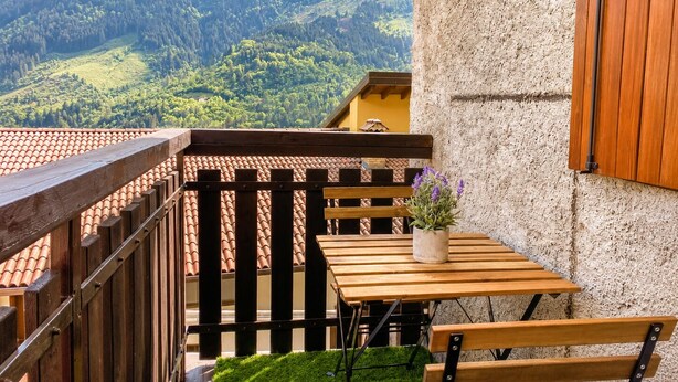 Un balcon avec une table et des chaises en bois, un pot de fleurs et une vue sur un paysage montagneux.