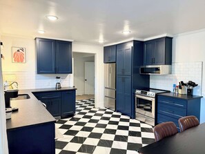 A kitchen with dark blue cabinets, a black and white checkered floor, and stainless steel appliances. - Charming Mid-Century Retreat | Pets Welcome (Raleigh)