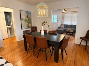 A dining area with a rectangular table, six chairs, a vase with plants, and a painting on the wall. - Charming Mid-Century Retreat | Pets Welcome (Raleigh)
