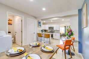 Una cocina moderna con armarios blancos, un microondas y una zona de comedor con mesa de madera y sillas naranjas.