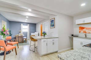 Una cocina moderna con armarios blancos, encimera de granito y comedor con sillas anaranjadas y una mesa de madera.