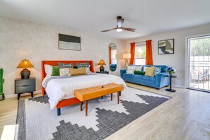 Ein Schlafzimmer mit einem Bett, Nachttischen, einer Bank, einem blauen Sofa, einem Deckenventilator und einem Fenster mit Vorhängen.