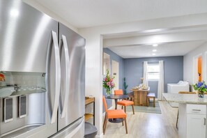 Una cocina moderna con un refrigerador de acero inoxidable, un comedor con sillas anaranjadas y una pequeña mesa con un jarrón de flores.