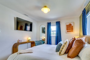 Una habitación de hotel con cama, mesita de noche, lámpara, espejo y cortinas.