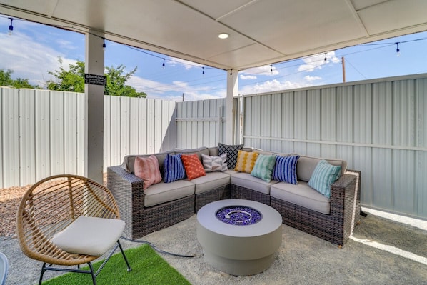 Un espacio de patio cubierto con un sofá modular, una mesa redonda y una silla de mimbre.