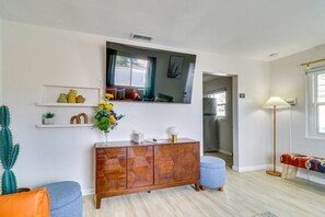Una sala de estar moderna con un mueble de madera, un cactus, un sofá azul, una lámpara de pie y un televisor montado en la pared.