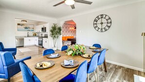 Una cocina moderna con armarios blancos, una zona de comedor con sillas azules, una mesa de madera y un reloj de pared.