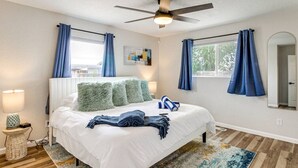 Un dormitorio con cama, ventilador de techo, ventana con cortinas, lámpara de noche y alfombra.
