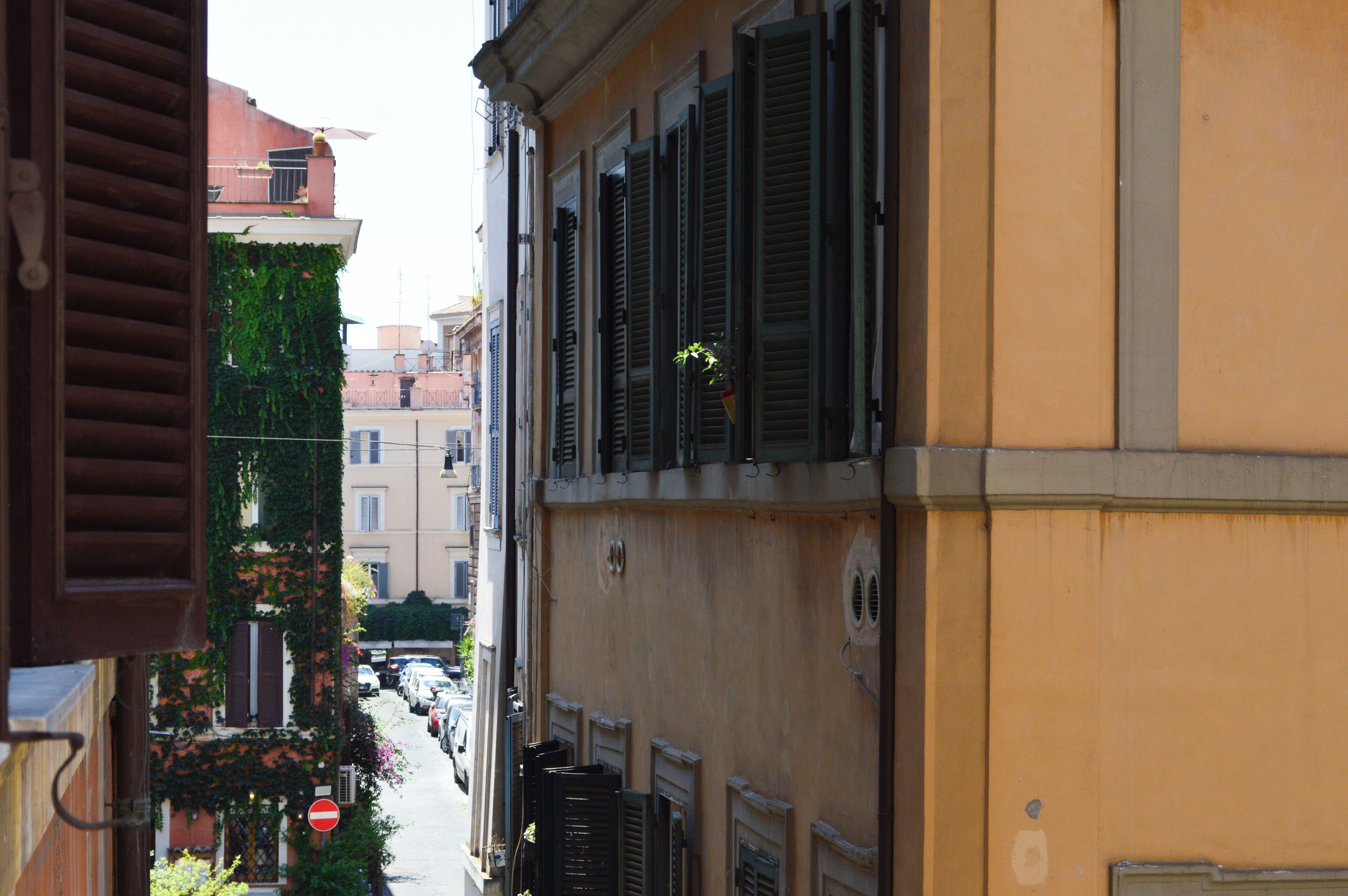 A narrow street with buildings on either side, closed shutters, and a no-entry sign.