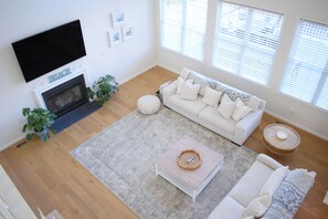 Ein Wohnzimmer mit Kamin, einem weißen Sofa, einem Couchtisch und einem an der Wand montierten Fernseher.