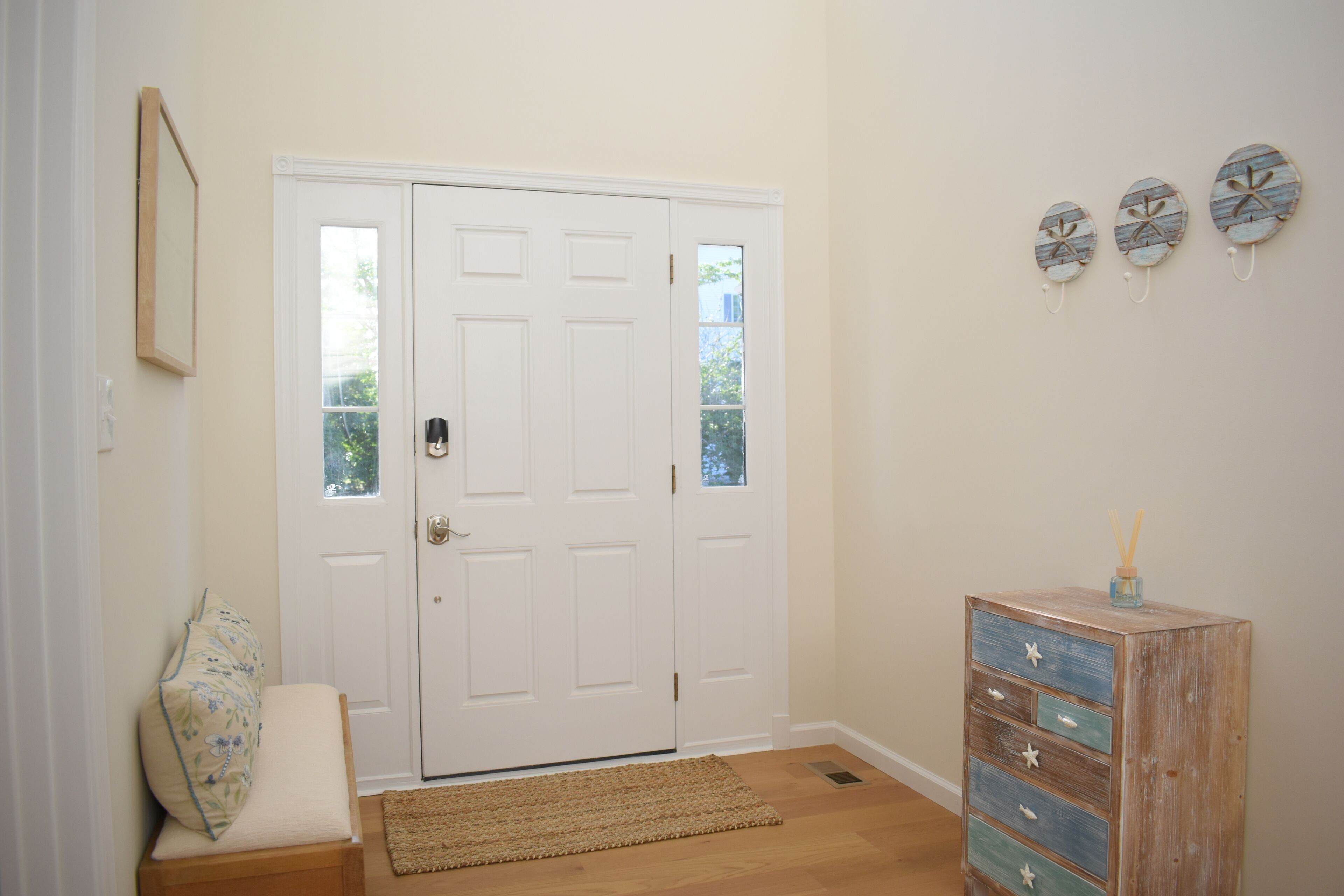 Una habitación con una puerta blanca, un banco de madera y un aparador con cajones.