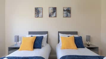 A hotel room with two beds, each with a nightstand, a lamp, and a picture frame on the wall.