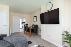 A modern bedroom with a bed, a TV mounted on the wall, and a dining area with chairs and a table. - Contractor Stay | Parking & Fast Wi-Fi | Sleeps 4 (Barton Seagrave)