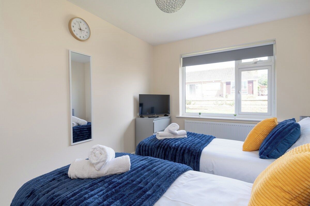 A hotel room with two beds, a television, a window, and a clock on the wall.