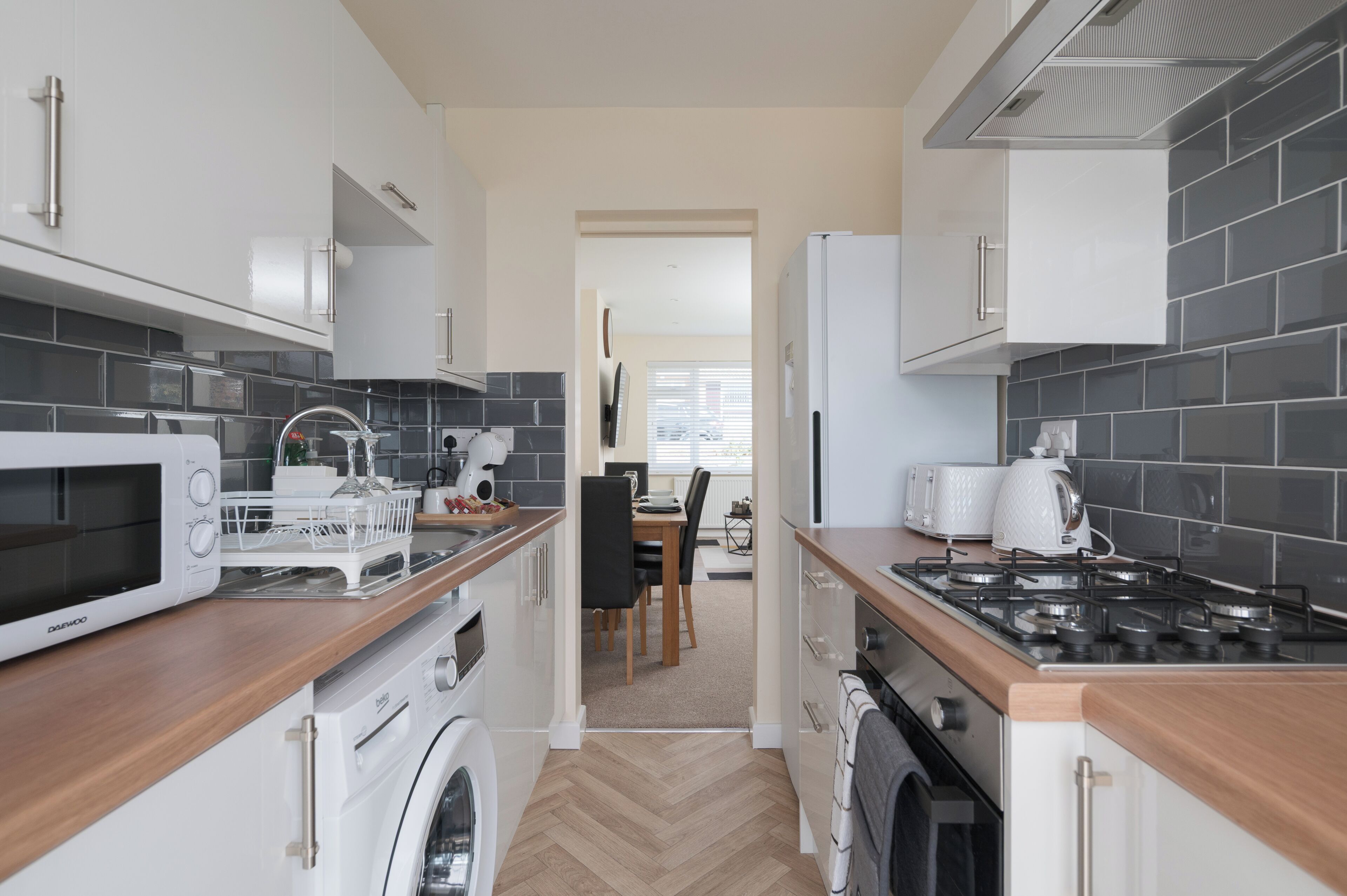 A compact kitchen with a microwave, toaster, and stove, leading to a dining area with a table and chairs.