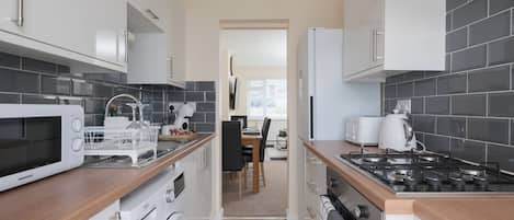 A compact kitchen with a microwave, toaster, and stove, leading to a dining area with a table and chairs.