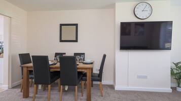 A dining area with a wooden table, black chairs, a clock, and a flat-screen TV mounted on the wall.