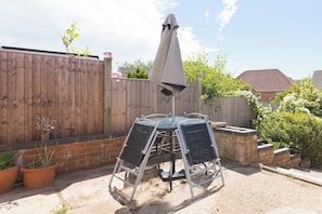 A patio with a metal table and chairs, a grey umbrella, and a wooden fence. - Contractor Stay | Parking & Fast Wi-Fi | Sleeps 4 (Barton Seagrave)