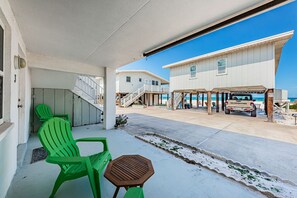 Een pand aan het strand met een overdekt terras, groene stoelen en een houten tafel.