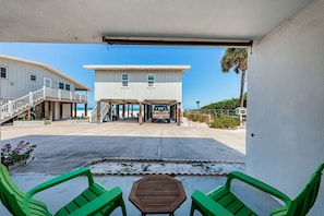 Ein überdachter Außenbereich mit Tisch und Stühlen, ein Gebäude mit Garage und freier Blick auf den Strand.