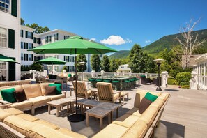 Une terrasse dotée de mobilier d’extérieur et de parasols, offrant une vue sur une piscine et un paysage montagneux.