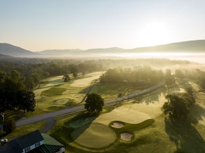 An aerial view of a golf course with multiple holes, pathways, and a distant mountain range. - Cozy Quarters | 2 Queen + Mountain View (Manchester)