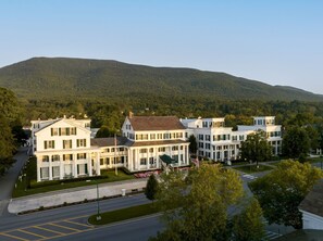Ein großes, weißes Gebäude mit mehreren Stockwerken und einer symmetrischen Fassade, umgeben von einer gepflegten Rasenfläche und einer Straße.