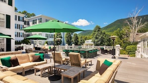 Eine Terrasse mit Gartenmöbeln und Sonnenschirmen, mit Blick auf einen Pool und eine gebirgige Landschaft.